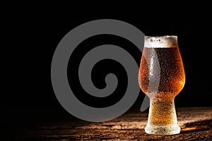 Beer. Cold Craft light Beer in a glass with water drops on the wooden table over the black background