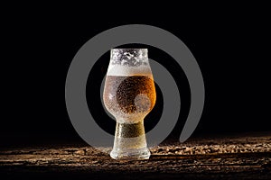 Beer. Cold Craft light Beer in a glass with water drops on the wooden table over the black background