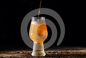 Beer. Cold Craft light Beer in a glass with water drops on the wooden table over the black background