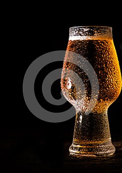 Beer. Cold Craft light Beer in a glass with water drops on the wooden table over the black background