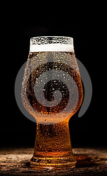 Beer. Cold Craft light Beer in a glass with water drops on the wooden table over the black background