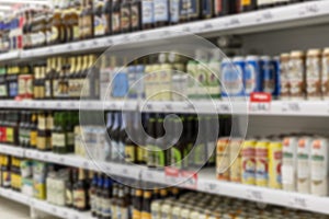 Beer of different brands in bottles and cans on the shelves in the supermarket. Large selection of alcoholic beverages. Blurred