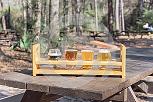 Beer flight sampler tray on wooden picnic table with blurry forest background of brewery in Texas, USA