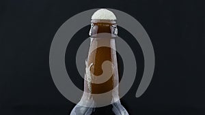 Beer foam flows down a misted bottle of beer. Beer foam flows down a bottle of dark beer.