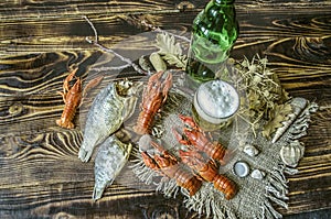 Beer with foam in a glass and a bottle of beer with a snack of boiled craw fish and dried salted fish