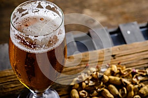 Beer glass with dark cold beer with bubble froth and peanuts on