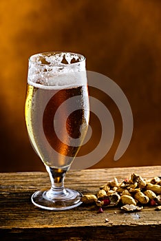 Beer glass with dark cold beer with bubble froth and peanuts on