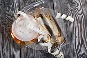 Beer in a glass and smoked fish. Nearby is a measuring tape. On pine boards. A day without diets