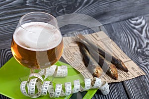 Beer in a glass and smoked fish. Scales and measuring tape are nearby. On pine boards. A day without diets