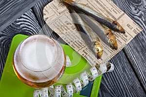 Beer in a glass and smoked fish. Scales and measuring tape are nearby. On pine boards. A day without diets