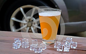 Beer in glass on wood table with ice, car background.