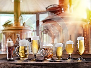 Beer glasses on wooden table and copper brewing cask at the background