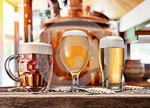 Beer glasses on wooden table and copper brewing cask at the background. Craft brewery