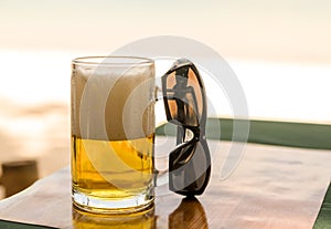 Beer with high white foam transparent mug sunglasses outdoor cafe lunch on a hot day