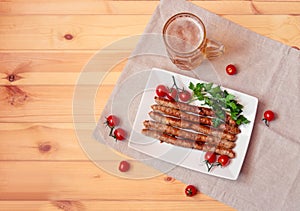Beer mug and plate with roasted sausages, cherry tomatoes and parsley on wooden table.