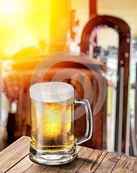 Beer mug on wooden table and copper brewing cask at the background