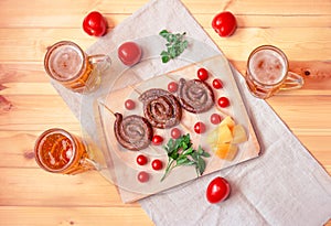 Beer mugs and cutting board with roasted sausages, cherry tomatoes, yellow pepper and fresh parsley on wooden table