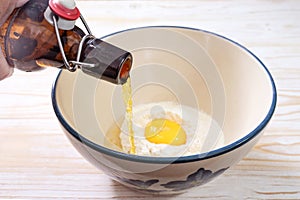 Beer is poured from a bottle into a bowl with flour, egg and oil to make a beer batter or dough to cover vegetables or fish for