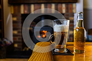 Beer poured into glass on oak table with log burner fire on background at home