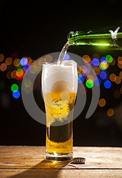 Beer is pouring into glass on bar lights background