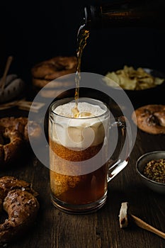 Beer pouring in glass with pretzels, bratwurst and snacks on rustic wooden table