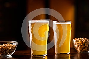 Beer set in pub. Two glasses of ale, nuts and pistachios on table in interior