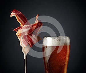 Beer and slices of  fried bacon on black background