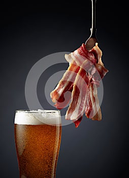 Beer and slices of  fried bacon on black background