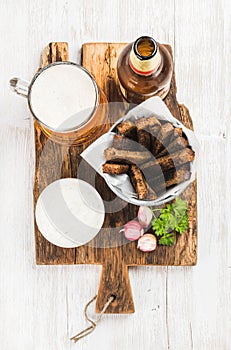 Beer snack set. Pint of pilsener in mug, open glass bottle, rye bread croutons with garlic cream cheese sauce on rustic photo