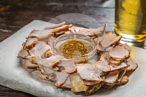 Beer snack of thinly sliced pieces of meat with a sauce of grainy mustard on the Board for filing is covered with a sheet of parch