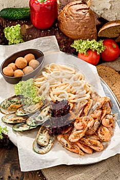Beer snacks: onion rings, mussels in a creamy sauce, fried shrimps and cheese balls on craft paper on a tray
