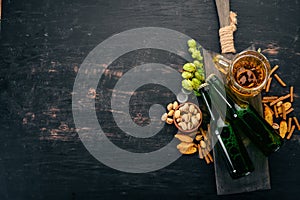 Beer and snacks. Salted crackers, Dried Fish, Chips, Nuts, Peanuts, Pistachios. On a black wooden background.