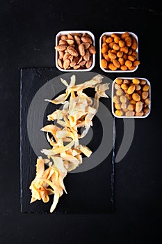 Beer snacks. Salty squid. Salted nuts in the assortment. Black background. Vertical photo. Copy space.Flat lay.
