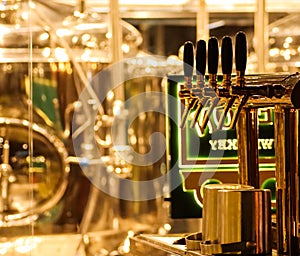 Beer taps to dispense beer in mug with selective focus and distillery in background of a brewery