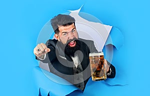 Beer time. Oktoberfest festival. Bearded man with craft beer looking through paper hole. Alcohol. Handsome man drinking