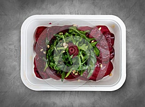 Beet carpaccio, arugula and nuts. Vegetarian food. Takeaway food. Top view, on a gray background