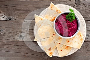 Beet hummus with pita bread on a plate over wood