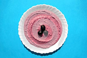 Beet hummus in a white plate on blue background.