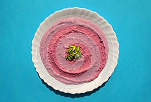 Beet hummus in a white plate on blue background