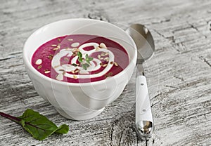 Beet soup in a white bowl on bright wooden surface