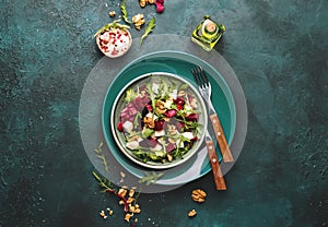 Beet summer salad with arugula, radicchio, soft cheese and walnuts on plate with fork, dressing and spices on blue kitchen table,