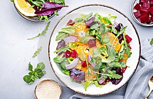 Beetroot, feta cheese and tangerine healthy salad with arugula, lettuce, red onion on gray kitchen table. Fresh useful dish for