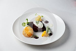 Beetroot terrine, goat cheese croquettes, horseradish sauce and dill cream on white dish