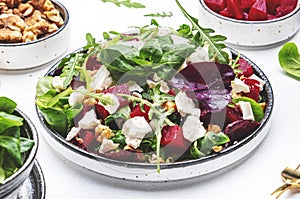 Beetroot and white cheese salad with arugula, lettuce, chard and walnuts, white table, copy space. Fresh useful vegetarian dish