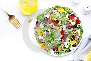 Beetroot and white cheese salad with arugula, lettuce, orange and pistachios on white table. Fresh useful dish for healthy eating