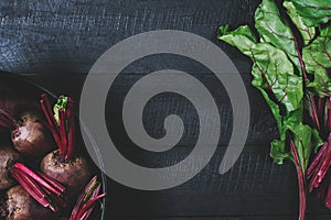 Beets with green tops in round metal pan on dark black wooden background, fresh red beetroot on backdrop kitchen table top view