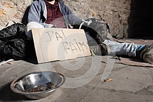 Beggar and dog sitting next to alms bowl on street