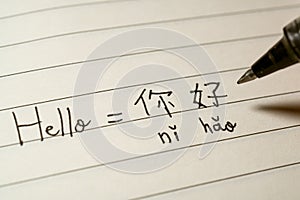 Beginner Chinese language learner writing Hello word Nihao in Chinese characters and pinyin on a notebook photo