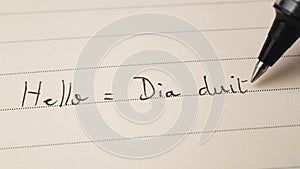 Beginner Irish Gaelic language learner writing Hello word Dia duit for homework on a notebook
