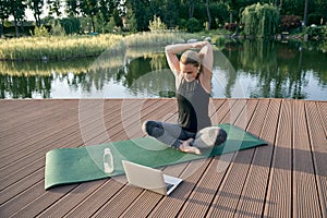 Beginner. Sporty beautiful woman exercising, watching instructional videos on a laptop while doing yoga on a mat in photo